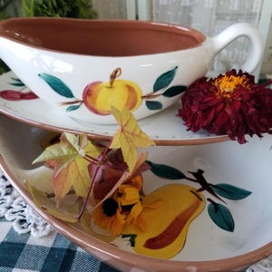 May include: A set of two vintage ceramic serving dishes with a brown rim and white interior. The dishes feature hand-painted fruit designs, including a red apple, a yellow pear, and green leaves.