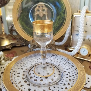 May include: A clear glass serving dish with a gold rim and intricate floral pattern. The dish is on a white crocheted doily and has a smaller clear glass dish inside.