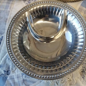 Puede incluir: Un conjunto de fuentes plateadas. Cada fuente tiene un compartimento central elevado y un borde con cuentas. Las fuentes son redondas y reflejan la luz, lo que sugiere una superficie pulida. El fondo es una tela estampada en azul claro y blanco.