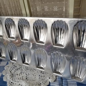 May include: A vintage silver metal baking pan with 10 individual molds for making small cakes or pastries. The molds have a fluted design.