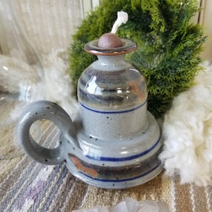 May include: A gray ceramic oil lamp with a blue and brown glaze. The lamp has a handle and a round base. It has a wick and a brown cap on top.