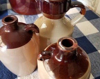 May include: Four brown and cream glazed ceramic jugs with a brown and white checkered background. The jugs are different sizes and shapes.