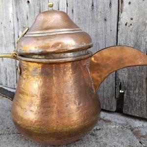May include: A vintage copper teapot with a brass handle and spout. The teapot has a hammered finish and a domed lid with a brass knob.