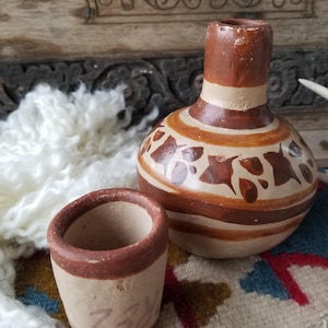 May include: A set of two brown and white ceramic pottery pieces. The larger piece is a jug with a wide base and a narrow neck. The smaller piece is a cup with a rounded base. Both pieces have a brown and white striped pattern with brown floral designs.