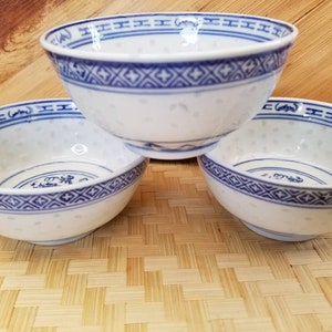 May include: Three white ceramic bowls with blue and white patterned designs. The bowls have a speckled glaze and a rounded shape.