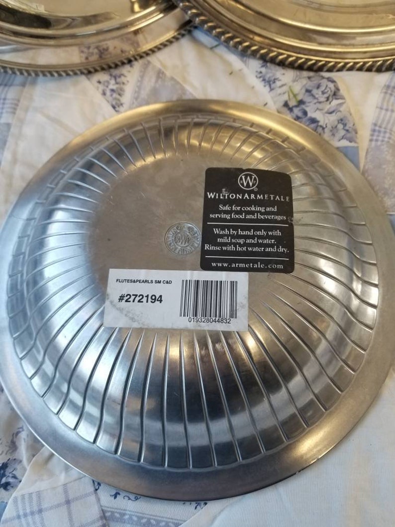 Puede incluir: Platos de servir de metal plateado con un dise&ntilde;o acanalado. Los platos tienen un borde decorativo y una etiqueta que dice "WILTON ARMETALE" y "FLUTES&PEARLS SM C&D #272194".