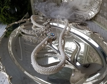 May include: A silver serving platter with a beaded necklace and a decorative brooch on top. The platter has a scalloped edge and ornate details.