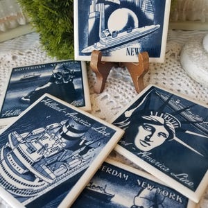 May include: Set of five blue and white ceramic tile coasters featuring a nautical theme. The coasters depict ships, the Statue of Liberty, and the New York City skyline. The text "Holland-America Line" is featured on four of the coasters.