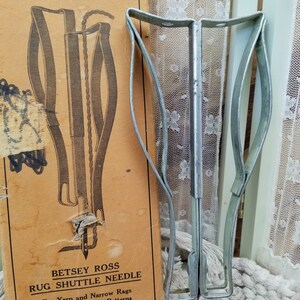 May include: An antique Betsey Ross rug shuttle needle with a metal frame and a vintage instruction booklet. The booklet is tan with black text and illustrations. The text reads "RUG SHUTTLE NEEDLE" and "For Yarn and Narrow Rags on Canvas or Rug Patterns."