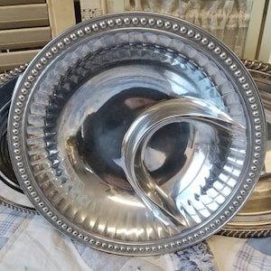 Puede incluir: Una fuente plateada con una secci&oacute;n en forma de media luna para salsas. La fuente tiene un borde con cuentas y un dise&ntilde;o acanalado alrededor del borde. La superficie reflectante de la fuente crea un efecto de espejo.