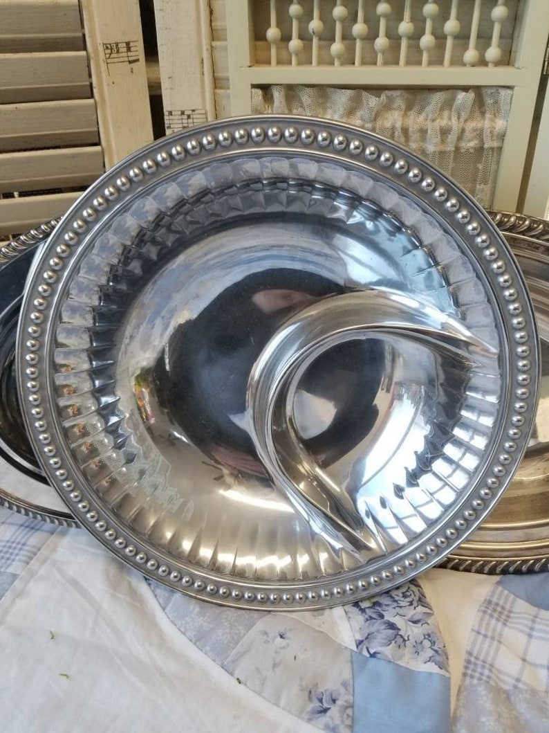 Puede incluir: Una fuente plateada con una secci&oacute;n en forma de media luna para salsas. La fuente tiene un borde con cuentas y un dise&ntilde;o acanalado alrededor del borde. La superficie reflectante de la fuente crea un efecto de espejo.