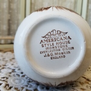 May include: A white ceramic mug with a brown Americana Style House Ironstone Everlasting Colour J&G Meakin England stamp on the bottom.