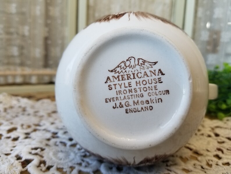 May include: A white ceramic mug with a brown Americana Style House Ironstone Everlasting Colour J&G Meakin England stamp on the bottom.