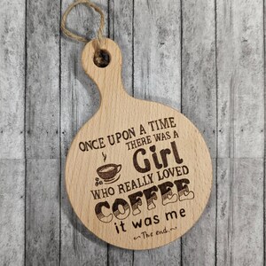 May include: Wooden coaster with a funny saying about coffee. It reads "Once upon a time there was a girl who really loved coffee it was me ~The end."