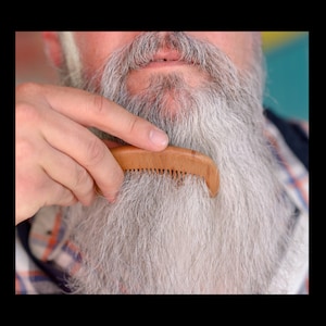 May include: A close-up of a man's long, white beard being combed with a wooden comb.