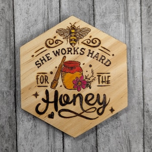 May include: Wooden hexagonal sign with a bee, a jar of honey, and flowers. The sign reads "She works hard for the honey".