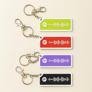 May include: Keychains with rectangular tags in green, red, purple, and black, each featuring a unique Spotify code. The keychains have silver-colored metal hardware, including a split ring and a lobster clasp for easy attachment.