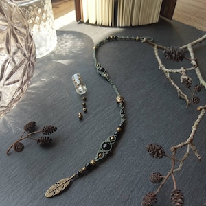 Peut inclure: Un collier de perles vertes et noires avec un petit pendentif en forme de plume dorée. Le collier comporte une perle de Bouddha et des perles noires.