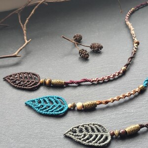 Peut inclure: Trois colliers en macramé en forme de feuille avec des perles en bois et en métal. Les feuilles sont brunes, bleu sarcelle et grises.