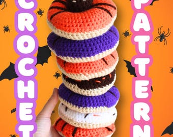 May include: A stack of colorful, crocheted donuts in orange, purple, white, and brown. The donuts are stacked vertically, with a hand holding the bottom donut. The background is orange with bats and spiders. Text on the left says "CROCHET" and on the right "PATTERN".