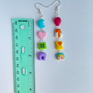 May include: A pair of dangle earrings with a rainbow, purple, green, pink, orange, and blue charm. The charms are attached to a silver hook.