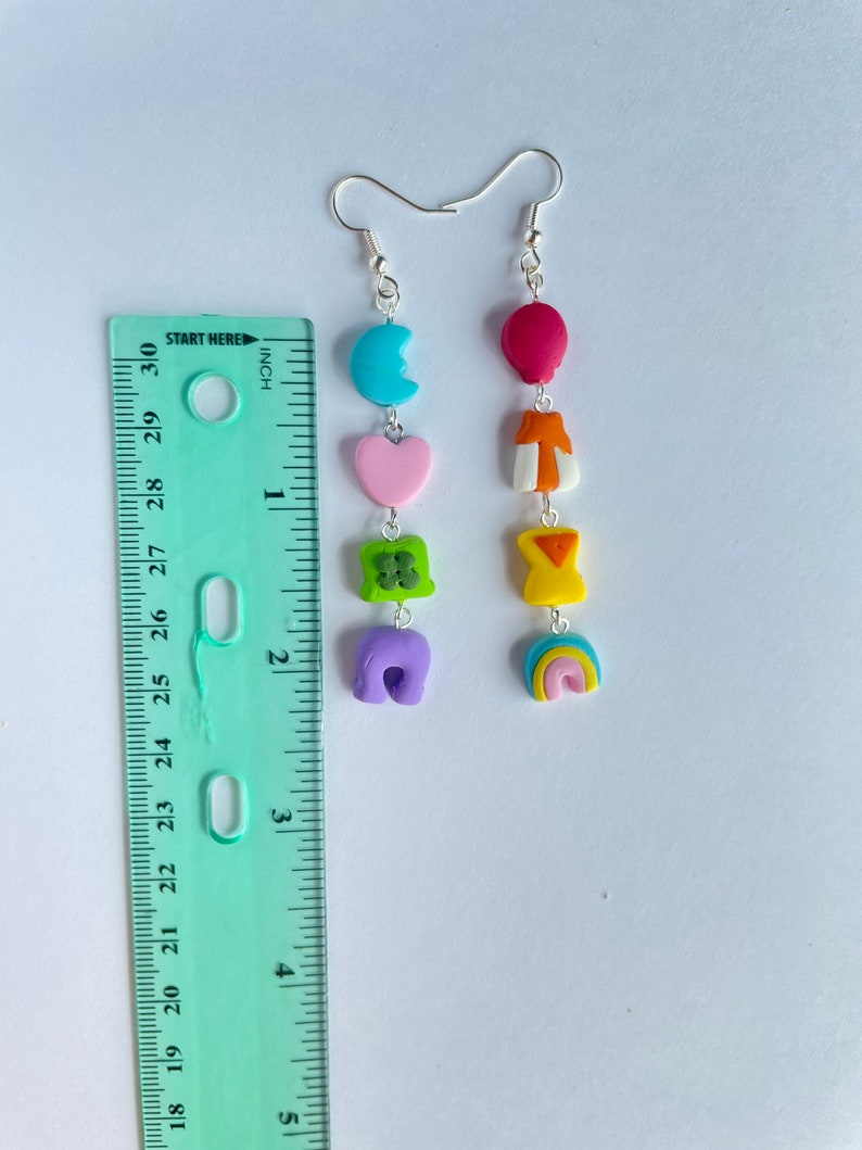 May include: A pair of dangle earrings with a rainbow, purple, green, pink, orange, and blue charm. The charms are attached to a silver hook.