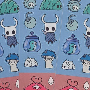 Puede incluir: Tres hojas de pegatinas con diseños de personajes de dibujos animados en un esquema de color azul y rojo. Las pegatinas representan personajes con cuernos, setas y otras ilustraciones caprichosas. Las hojas están colocadas sobre una superficie de cuadrícula negra.