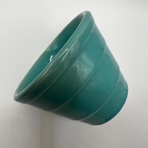 May include: A teal ceramic planter with a rounded shape and a slightly flared rim. The planter has a smooth, glossy finish and is perfect for displaying small plants or succulents.