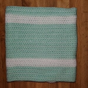 May include: A crocheted throw blanket with a green and white striped pattern. The blanket is made with a textured stitch and has a soft, cozy feel.