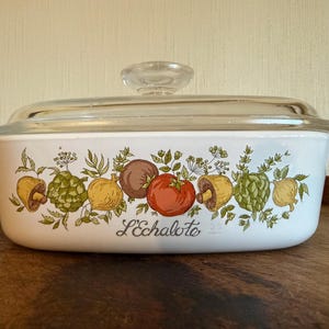 May include: Rectangular white casserole dish with a clear glass lid. The dish is decorated with colorful illustrations of vegetables and the text "L'Echalote". The dish has two small handles and is suitable for baking and serving.