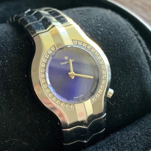 Op de afbeelding: Een zilveren en gouden Tag Heuer horloge met een blauwe wijzerplaat en diamanten accenten rond de bezel. Het horloge heeft een roestvrijstalen band met een schakellink-ontwerp.