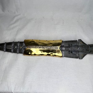 May include: A long, silver spear with a gold-plated section in the middle. The gold section has an inscription that reads "AUDENTES FORTUNA IUVAT".