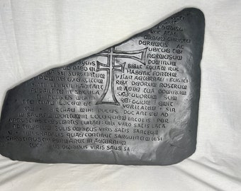 May include: A gray stone with a cross carved into it and an inscription in an old language. The inscription reads: "yclis GO DABO EI CASE SURGENTEIM DODINE EXERCICCIOL EYATI ILLI YOL HABITANT AUDARC CELIN SICULA CA DEUS E/S DE CC CUA LICE + RISTI 28 DEDISU RUC ACAE ARBEN CHRISECI DEAREQCIS AC UBICUG TIBI NERMASU DOMINCIM BIBIT AQUAM RUC HABIBIC FORTEIQ VILAG AGICERRAE: ECIGICH REX DEORUM ROSTRCIW IN ADDA TUA DOWINCI SAECOLORCI SIN REIFOGICION EDIT VORITATED SIR DOC ART WEI AD INCOL IS POR STR CHAE MIH! DUCEIS SACRAL WORCE@IN LOCO que ARGUSTIAS CRESCENTIS LUNAEI: UNI VIRO SATIS LACA AD TEMPLUM SOLIS OMNIBUS VIRIS SATIS SARCEG UBI GRADALIS QUAGI CONTINEIT SARGUIREI (ESI CHRISTIROSCRIPERWAREIT IN AGITEIRREIO US OQRIBUS VIRIS SAUS SA"
