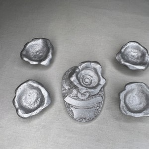 May include: Five silver-colored metal trinket dishes, each with a slightly different shape, and a silver-colored metal rose-shaped trinket dish with a decorative design.