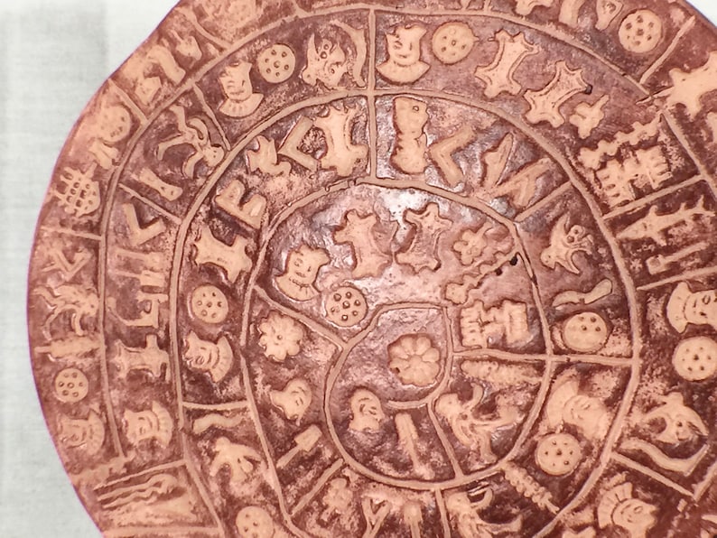 May include: A circular terracotta plate with a spiral design of various symbols and patterns. The plate is decorated with a repeating pattern of small circles, stars, and other geometric shapes.