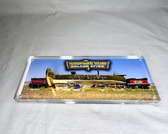 May include: A framed photograph of a golden spike, the "Golden Spike", with the text "Transcontinental Railroad Golden Spike" above it. The spike is resting on top of a train engine, with the text "Driving the Last Spike" on the side of the engine. The train is on a track in a field with a blue sky in the background.