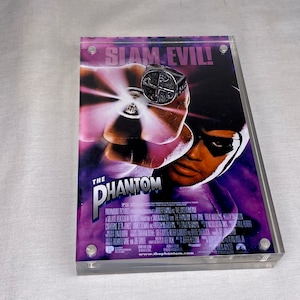 May include: A silver ring with a skull and crossbones design, displayed on a poster for the movie "The Phantom" with the text "Slam Evil!" on the poster.