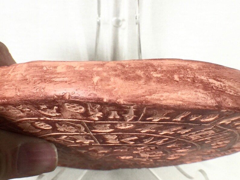 May include: A terracotta-colored circular disc with intricate carvings and designs. The disc is slightly raised in the center and has a smooth, slightly textured surface.