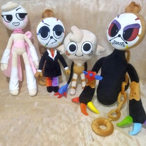 Peut inclure: Plusieurs poup&eacute;es en peluche faites &agrave; la main avec des visages expressifs uniques. Chaque poup&eacute;e pr&eacute;sente un design distinct, avec des tenues et des accessoires vari&eacute;s, dont un costume noir, une cape rose et une queue color&eacute;e. Les poup&eacute;es sont en tissu doux et ont des traits faciaux d&eacute;taill&eacute;s.