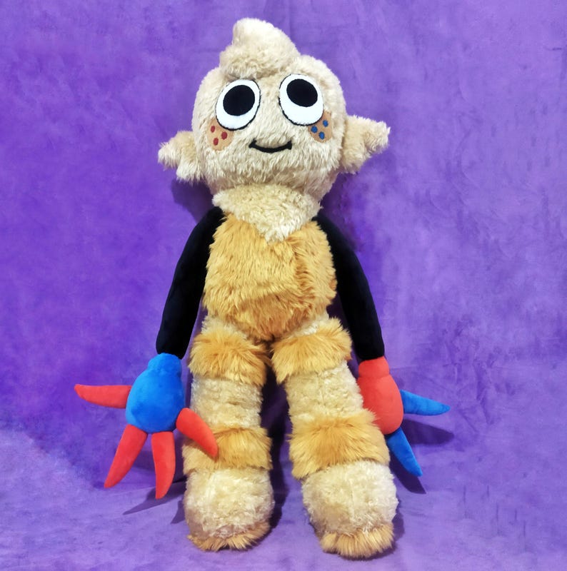 Peut inclure: Une peluche repr&eacute;sentant une cr&eacute;ature avec une t&ecirc;te et un corps beiges, des bras noirs et des jambes beiges et poilues. La cr&eacute;ature a de grands yeux noirs, des mains rouges et bleues et un visage souriant. Le fond est violet uni.