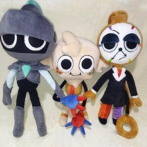 Peut inclure: Trois poup&eacute;es en peluche aux traits de dessins anim&eacute;s. La premi&egrave;re est grise avec un casque. La seconde est beige et tient un jouet en forme d'&eacute;toile bleu et rouge. La troisi&egrave;me porte un costume noir et a un visage d'horloge.