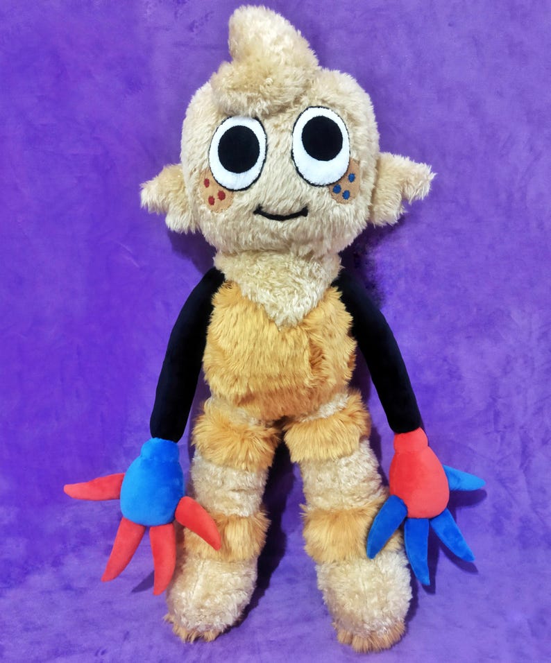 Peut inclure: Une peluche repr&eacute;sentant une cr&eacute;ature avec un corps brun clair et poilu, de grands yeux noirs et blancs et de petites oreilles. Elle a des bras noirs et des mains bleues et rouges. Le jouet est sur un fond violet.