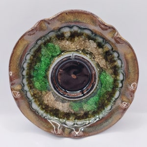 May include: A brown ceramic dish with a scalloped edge and a center well. The dish is decorated with green and gold accents.