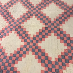 May include: A large, handmade quilt with a repeating pattern of pink and blue squares against a white background. The quilt's design features diagonal rows of alternating colors, creating a checkerboard effect. The quilt is likely made of cotton.