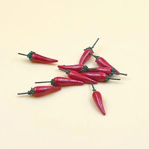 Puede incluir: Un grupo de diez chiles rojos con tallos verdes, esparcidos sobre una superficie beige claro.