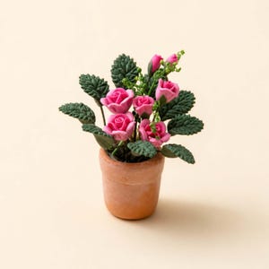 May include: A miniature terracotta pot filled with pink roses and green leaves. The roses are in full bloom, with several buds and small green sprigs. The pot is a light brown color, and the background is a solid cream color.