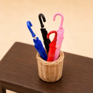 May include: A collection of miniature umbrellas in a woven basket. The umbrellas are in various colors: blue, black, red, and pink. The basket is made of light brown wicker and sits on a dark brown surface.