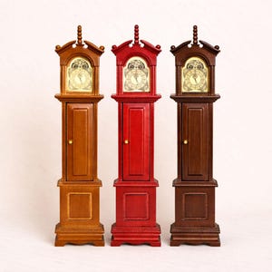 Peut inclure: Trois pendules grand-père miniatures en nuances de marron et de rouge. Chaque horloge présente un cadran détaillé et une petite porte. Les horloges sont en bois et ont un design classique.