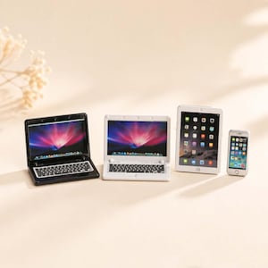 Pode incluir: Miniaturas de laptops em preto e branco, um tablet e um smartphone. As telas dos laptops exibem um design abstrato colorido. O tablet e o smartphone têm ícones de aplicativos. Os itens estão dispostos em uma superfície clara.