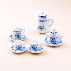 May include: A miniature porcelain tea set with a white base and blue floral designs. The set includes a teapot, a creamer, a sugar bowl, and three teacups with matching saucers. The tea set is designed for a dollhouse or miniature display.